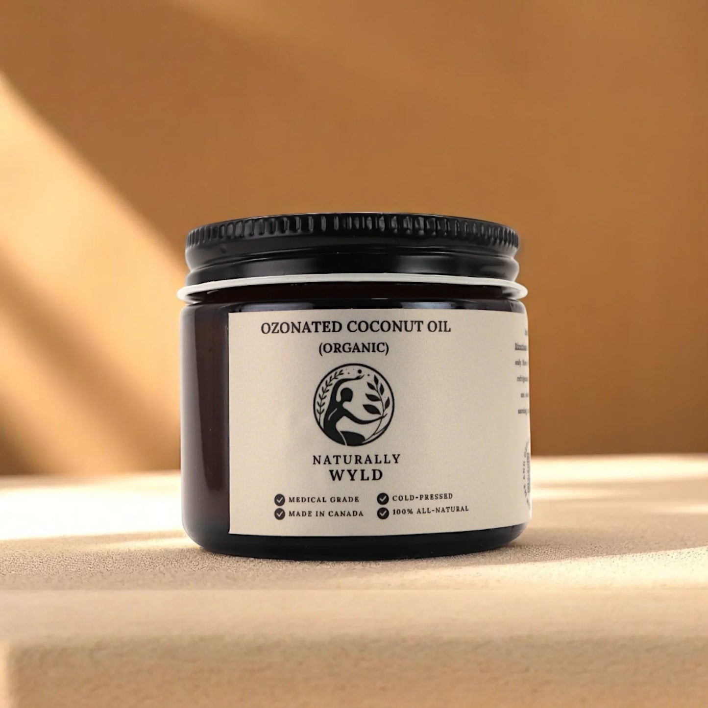 Naturally Wyld ozonated coconut oil in amber glass jar placed on a warm-toned natural surface with soft lighting – visually appealing product shot emphasizing minimalist, organic skincare and small-batch wellness made in Canada.