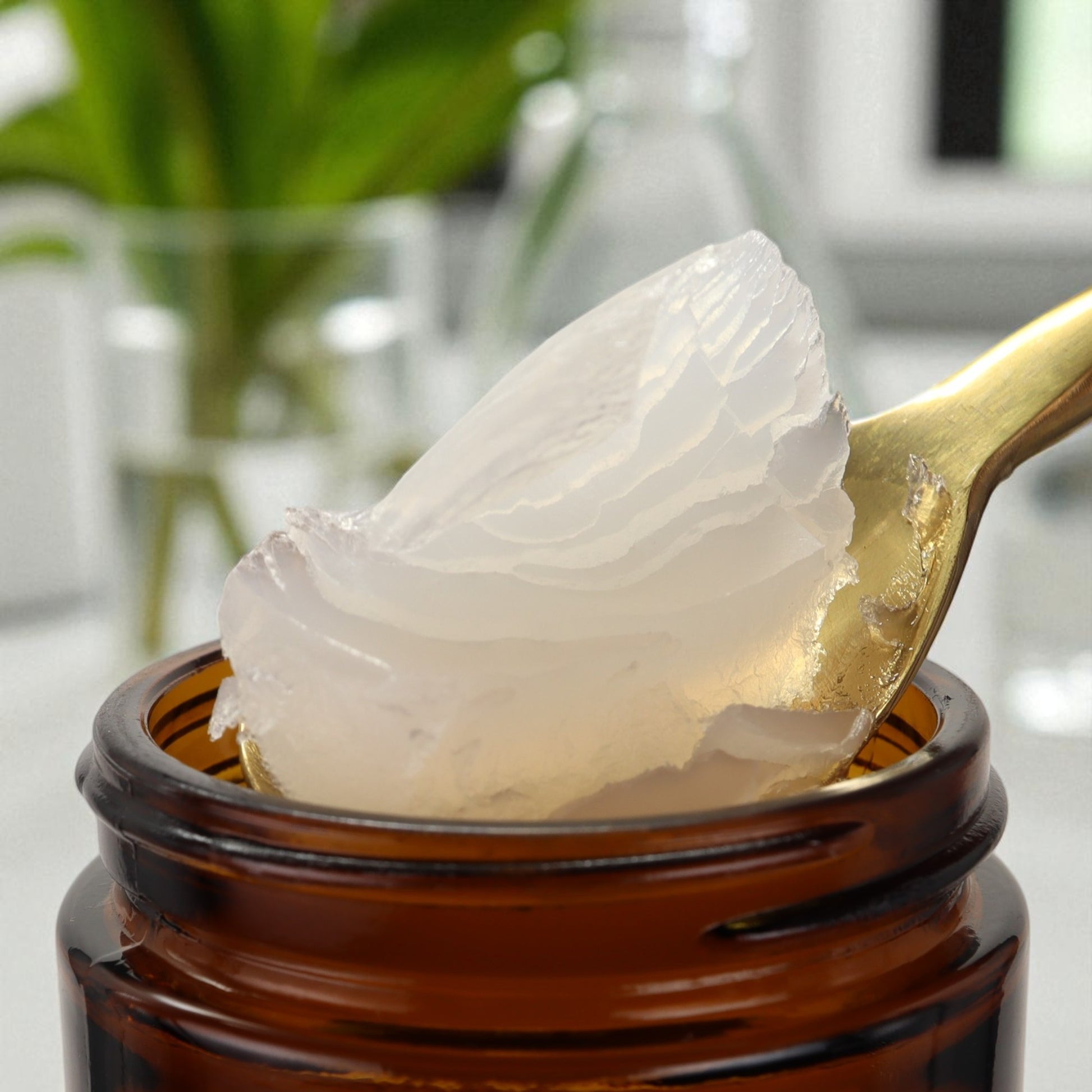 Close-up of a spoon with white cream being taken from an amber glass jar, with a blurred indoor background. Ozonated Olive Oil 