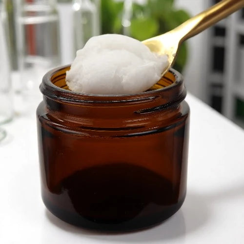 Thick ozonated coconut oil scooped from amber glass jar with golden spoon, highlighting its rich, creamy texture and natural skincare quality.