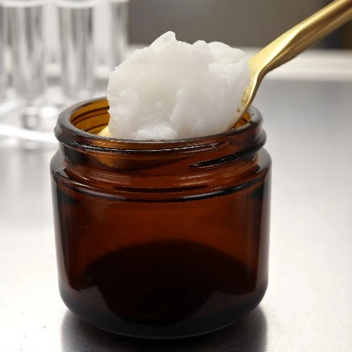 Golden spoon scooping ozonated jojoba oil from amber jar in lab setting, showcasing thick texture and premium small-batch skincare quality.